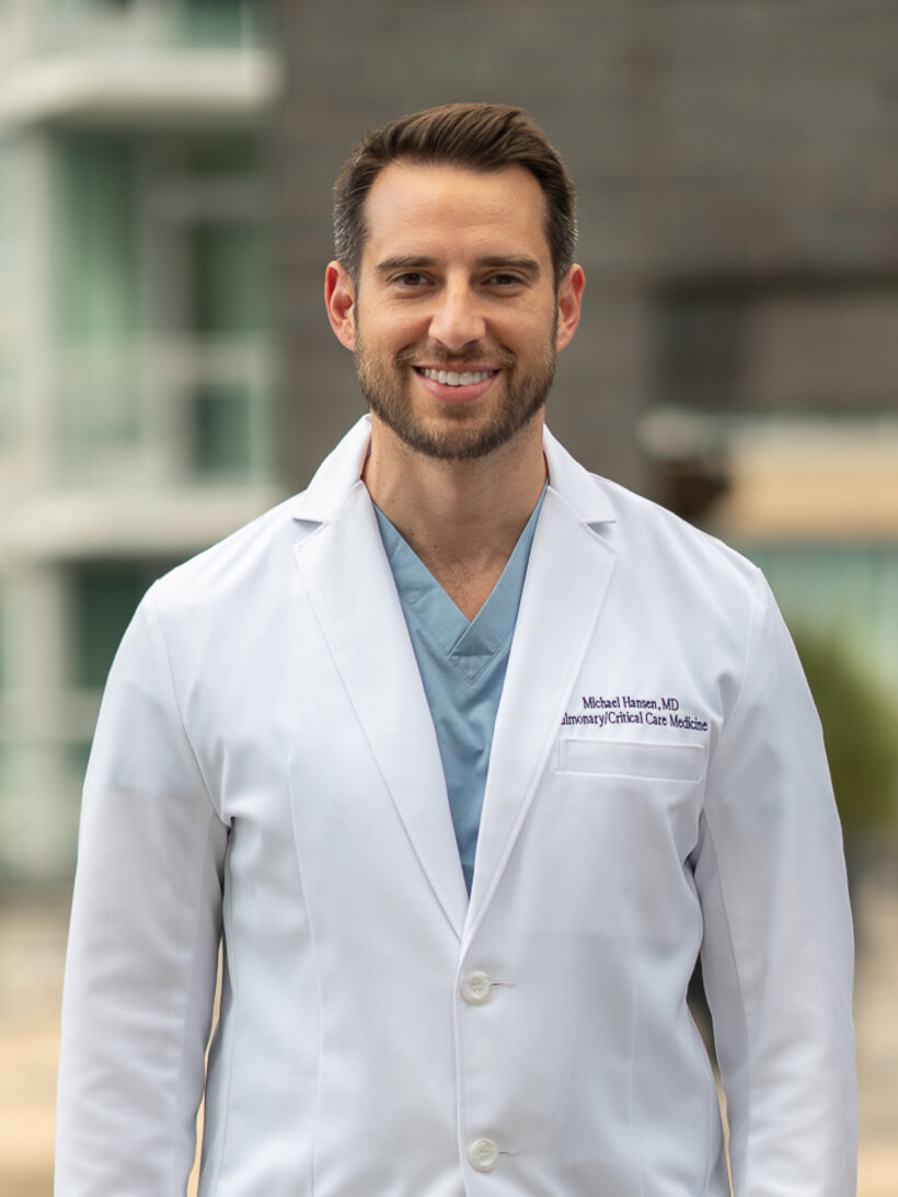 Michael Hansen, MD, in a white coat over scrubs